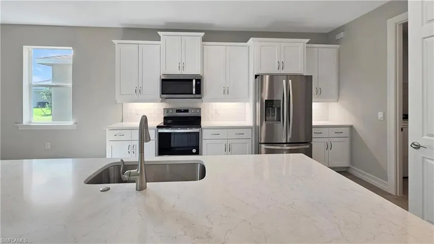 Kitchen featuring sink, stainless steel appliances, decorative backsplash, and light stone counters