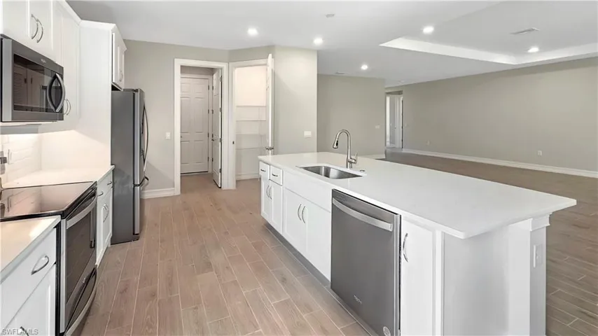 Kitchen featuring stainless steel appliances, light hardwood / wood-style floors, white cabinetry, sink, and a center island with sink