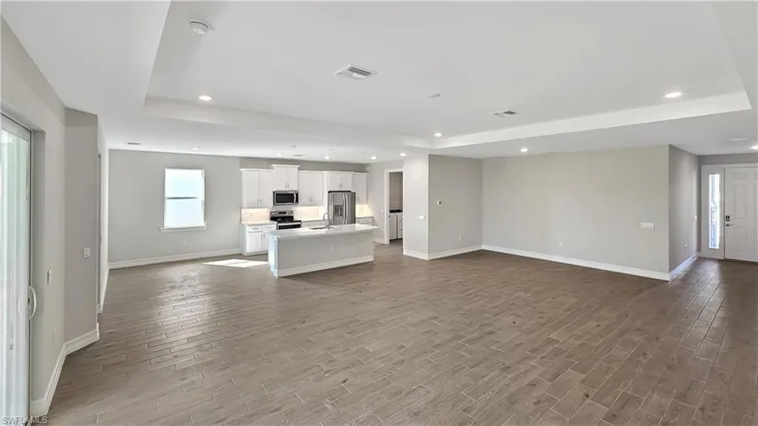 Unfurnished living room featuring sink, light hardwood / wood-style flooring, and a tray ceiling