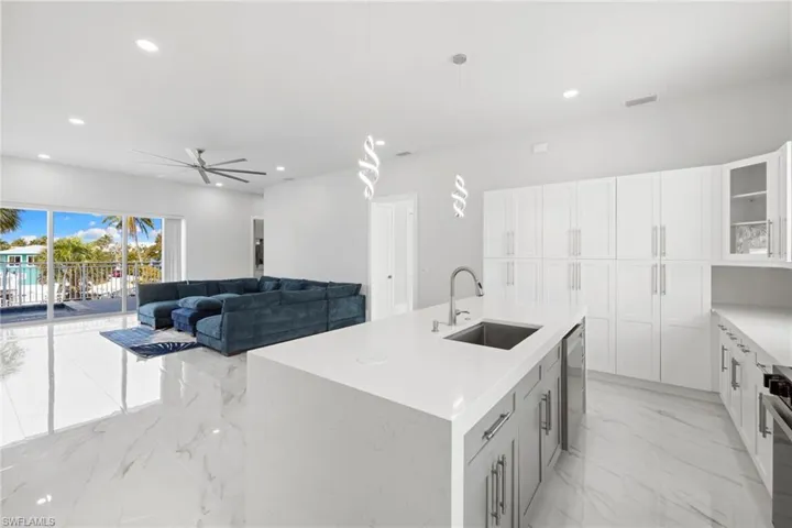 Kitchen featuring a kitchen island with sink, glass fronted cabinets, a ceiling fan, decorative light fixtures, and light stone countertops