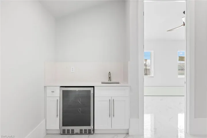 Indoor wet bar with beverage cooler, white cabinetry, light marble finish floors, and light stone counters