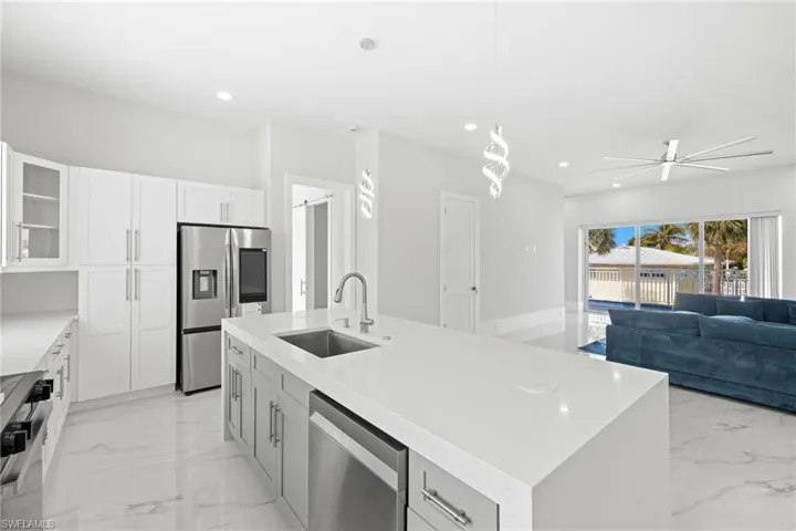 Kitchen with glass fronted cabinets, stainless steel appliances, a kitchen island with sink, and white cabinetry