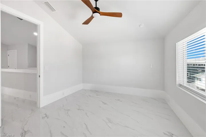 Spare room featuring light marble finish flooring, lofted ceiling, and ceiling fan