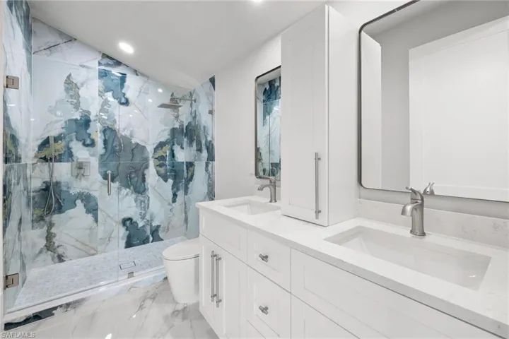 Full bathroom featuring double vanity, a marble finish shower, recessed lighting, and light marble finish floors