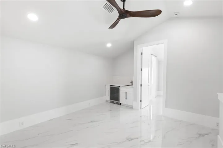 Unfurnished room with beverage cooler, recessed lighting, a ceiling fan, light marble finish flooring, and lofted ceiling