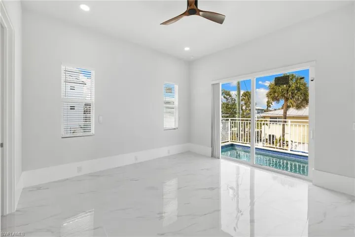 Spare room featuring a ceiling fan, healthy amount of natural light, light marble finish flooring, and recessed lighting
