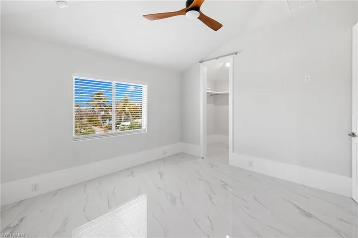 Unfurnished bedroom with a spacious closet, ceiling fan, vaulted ceiling, and light marble finish floors