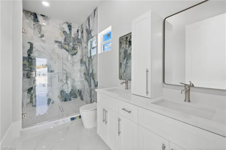 Full bathroom featuring double vanity, a marble finish shower, and light marble finish flooring