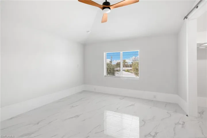 Unfurnished room featuring light marble finish floors, a ceiling fan, and lofted ceiling