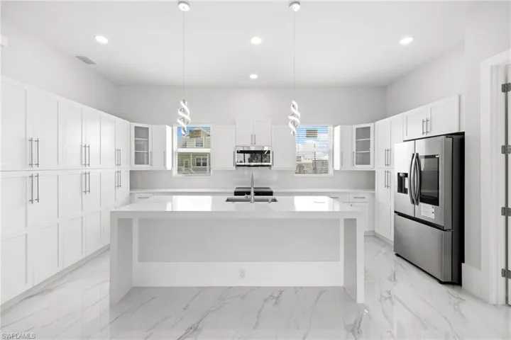 Kitchen with glass insert cabinets, stainless steel appliances, a kitchen island with sink, and light stone counters