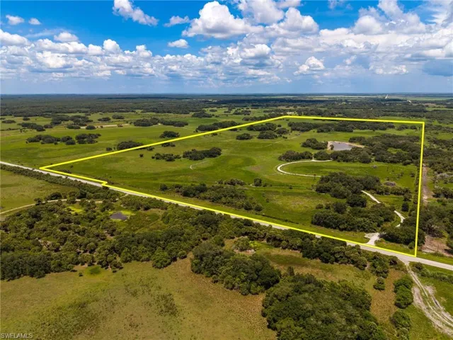 Expansive land parcel featuring a private pond, open pastures, mature tree clusters, and direct road frontage