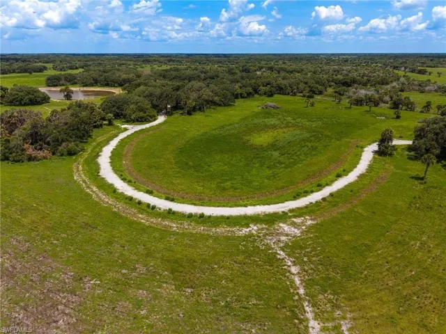 Expansive green acreage featuring a winding gravel path, mature trees, and a visible pond