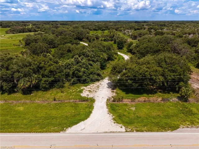 Expansive land parcel featuring an established road entrance, a winding internal path, mature trees, open grassy areas, and power lines