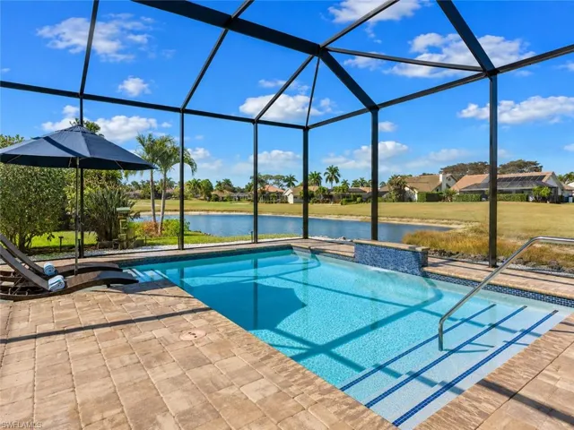Screened-in outdoor living space featuring a rectangular pool with integrated spa and waterfall, surrounded by paver decking and a tranquil water feature