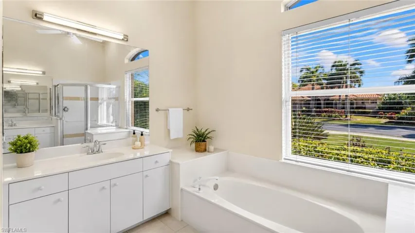 Master Bath featuring a built-in tub, white vanity with dual sinks, and a large window with blinds
