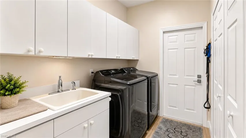 Laundry room featuring white cabinetry, a utility sink with chrome fixtures, a full-size washer and dryer, and wood-finish flooring