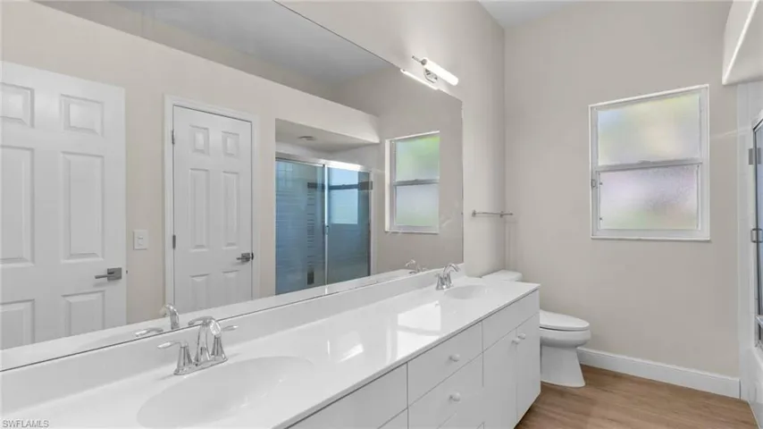 Full guest bathroom #2 with double vanity, light wood-style flooring, and enclosed tub / shower combo