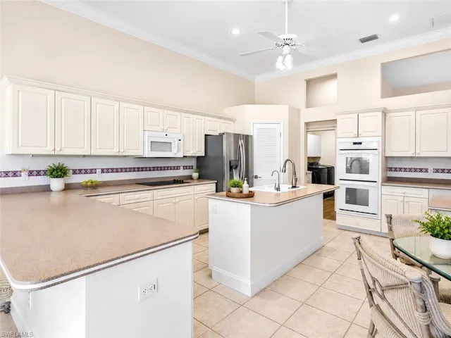 Open-concept kitchen featuring extensive cream cabinetry, a central island with an integrated sink, built-in double ovens, and tile flooring