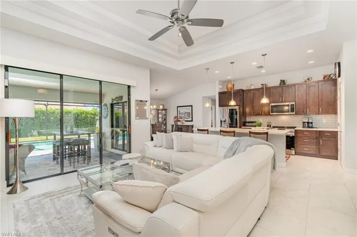 Living room with a raised ceiling, crown molding, light tile patterned flooring, ceiling fan, and a chandelier