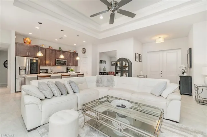 Living area featuring a tray ceiling, recessed lighting, light tile patterned flooring, ornamental molding, and ceiling fan