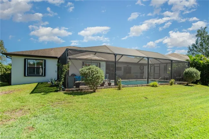 Rear view of property featuring a lanai, an outdoor pool, stucco siding, and a yard
