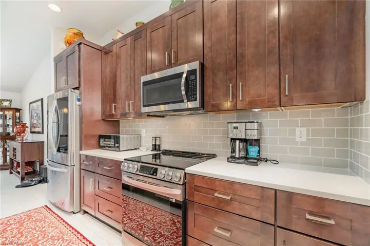Kitchen with appliances with stainless steel finishes, tasteful backsplash, lofted ceiling, and light tile patterned floors