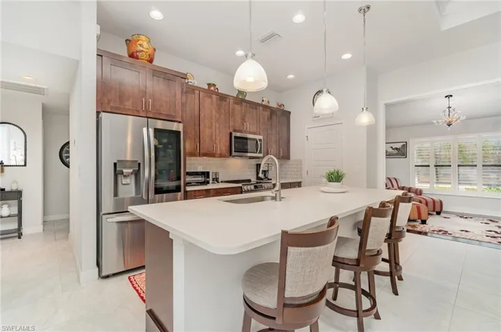 Kitchen featuring stainless steel appliances, tasteful backsplash, a center island with sink, pendant lighting, and a kitchen bar