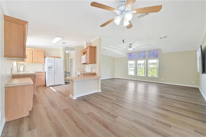 Kitchen featuring white appliances, light hardwood / wood-style floors, ornamental molding, light brown cabinets, and ceiling fan
