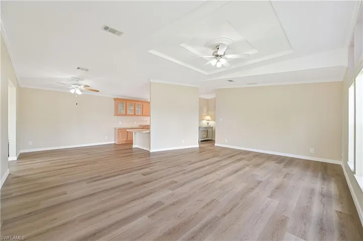 Unfurnished living room with a tray ceiling, ceiling fan, crown molding, and light hardwood / wood-style flooring