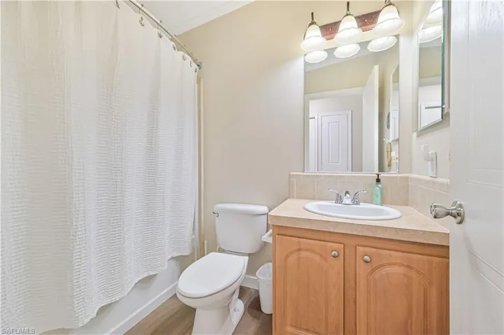 Full bathroom with backsplash, shower / bathtub combination with curtain, toilet, wood-type flooring, and vanity