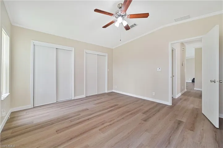 Unfurnished bedroom with crown molding, light hardwood / wood-style flooring, two closets, and ceiling fan