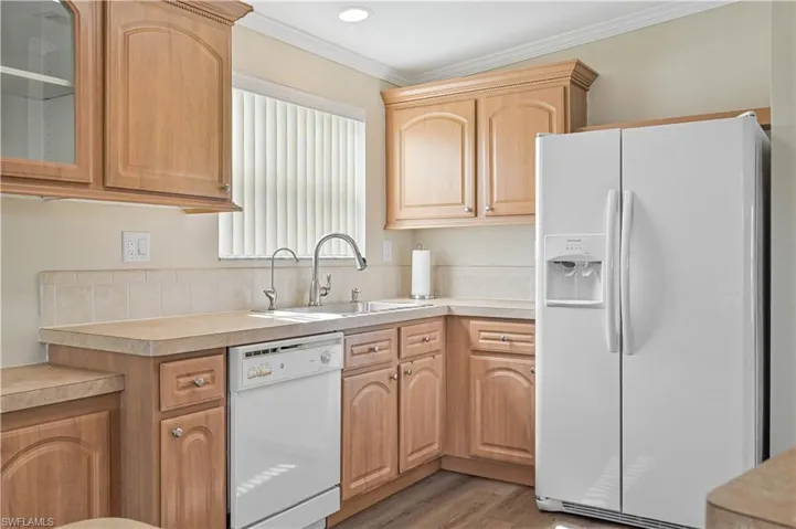 Kitchen with white appliances, light hardwood / wood-style flooring, crown molding, sink, and light brown cabinets