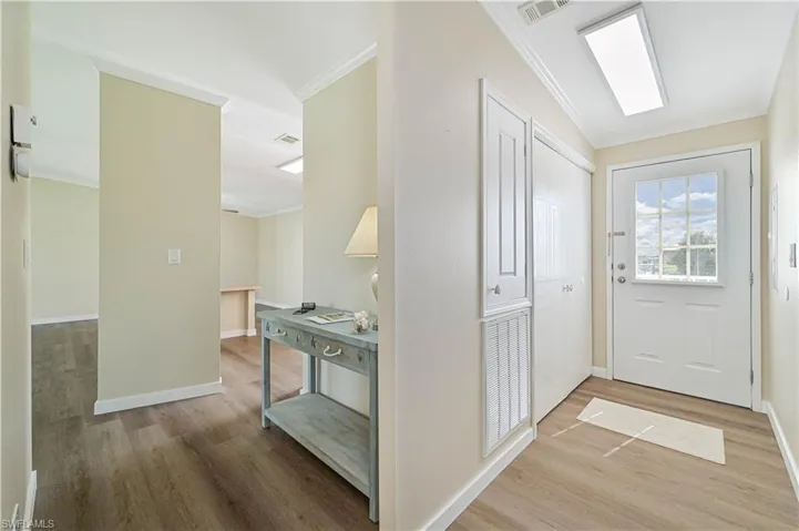 Entryway with ornamental molding, hardwood / wood-style flooring, and lofted ceiling with skylight