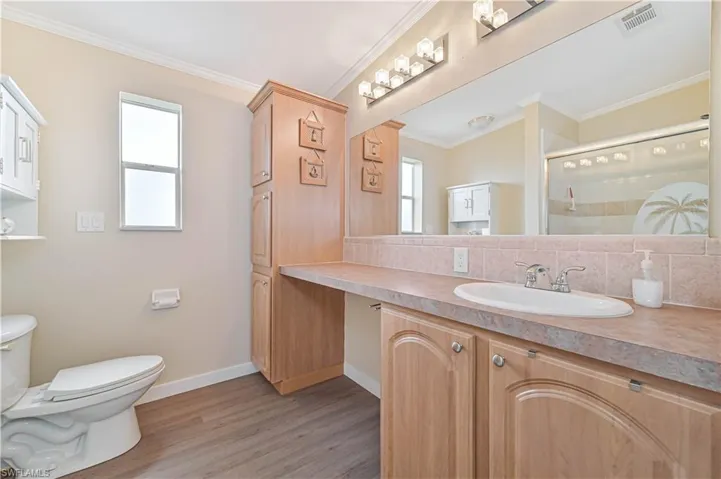 Bathroom featuring a shower with door, crown molding, toilet, wood-type flooring, and vanity