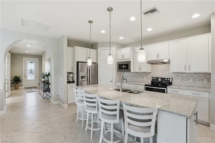 Kitchen with tasteful backsplash, white cabinetry, arched walkways, a breakfast bar area, and recessed lighting