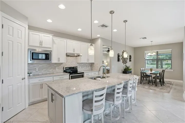 Kitchen featuring backsplash, a breakfast bar, stainless steel appliances, hanging light fixtures, and light stone counters