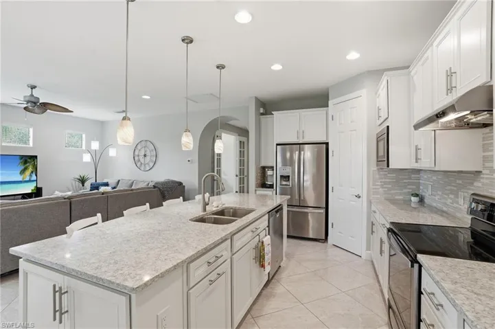 Kitchen with appliances with stainless steel finishes, arched walkways, white cabinetry, backsplash, and decorative light fixtures