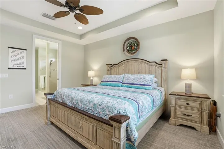 Bedroom with a raised ceiling, ceiling fan, light carpet, ensuite bathroom, and recessed lighting