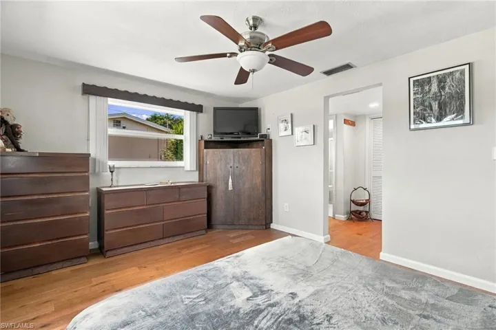 Room featuring wood-finish flooring, a multi-blade ceiling fan with integrated lighting, and a horizontal window with a valance