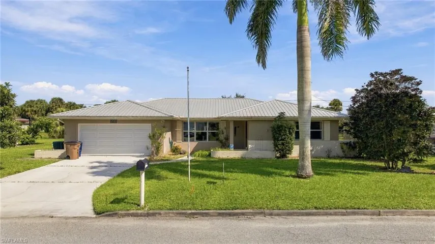 Single-story exterior featuring a metal roof, attached two-car garage, concrete driveway, and mature landscaping