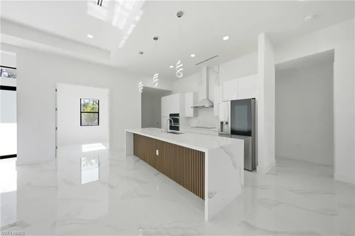 Kitchen with a large island with sink, two tone color scheme, light stone counters, stainless steel appliances, and decorative light fixtures