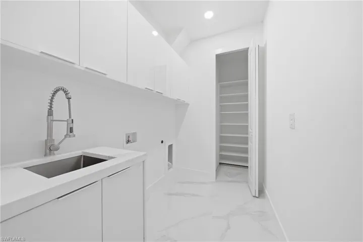 Utility room featuring a stainless steel sink with a high-arc faucet, extensive white cabinetry, white countertop, and white tile flooring