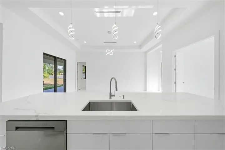Kitchen with a raised ceiling, light stone counters, dishwashing machine, open floor plan, and modern cabinets