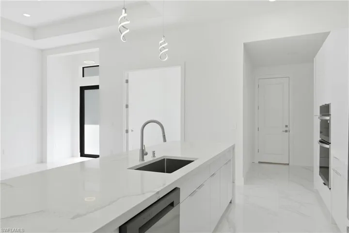 Kitchen with a raised ceiling, light stone counters, dishwashing machine, open floor plan, and modern cabinets