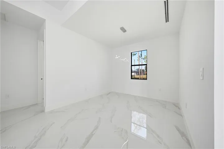 Spacious room featuring large format white and gray marble-look floor tiles, a single window with black trim, and a contemporary ceiling light fixture