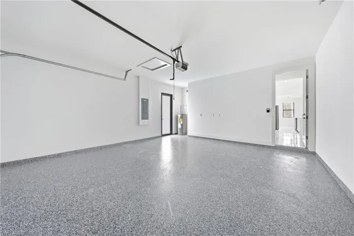 Spacious garage featuring a speckled epoxy floor, white walls, and a visible electrical panel