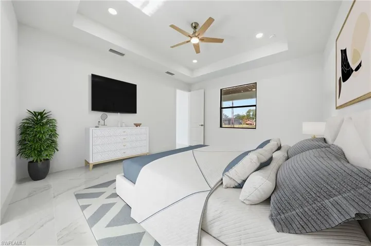 Spacious bedroom featuring a tray ceiling with recessed lighting and a ceiling fan, white walls, large format tile flooring, and a window with black trim