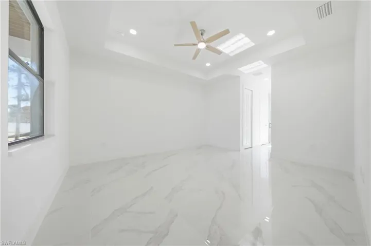 Spacious room featuring large format tile flooring, a tray ceiling, recessed lighting, a modern ceiling fan, and a deep-set window