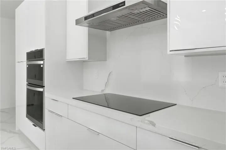 Sleek kitchen featuring built-in double ovens, a flush-mount cooktop, and a stainless steel range hood