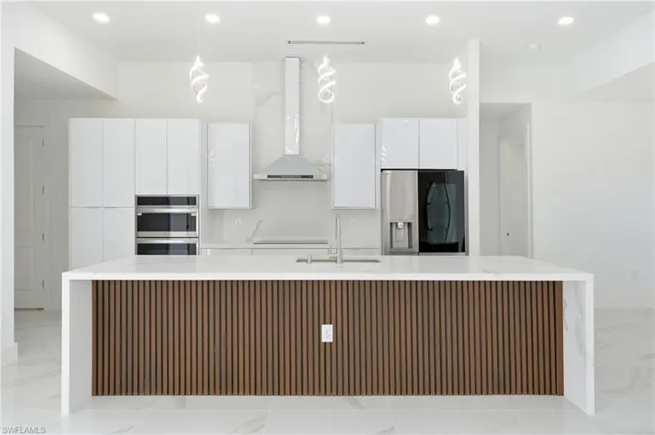 Dual tone kitchen with a center island with sink, two tone cabinets, light stone countertops, stainless steel appliances, and modern cabinets